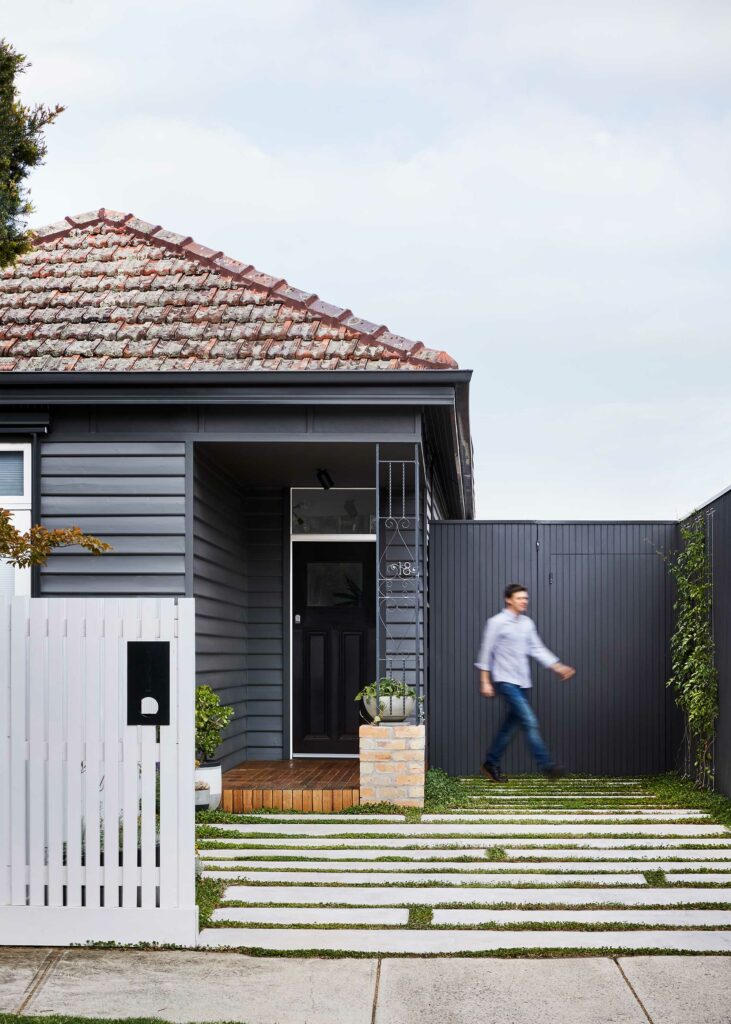 Maike Design weatherboard exterior painted charcoal. Concrete path with planting.