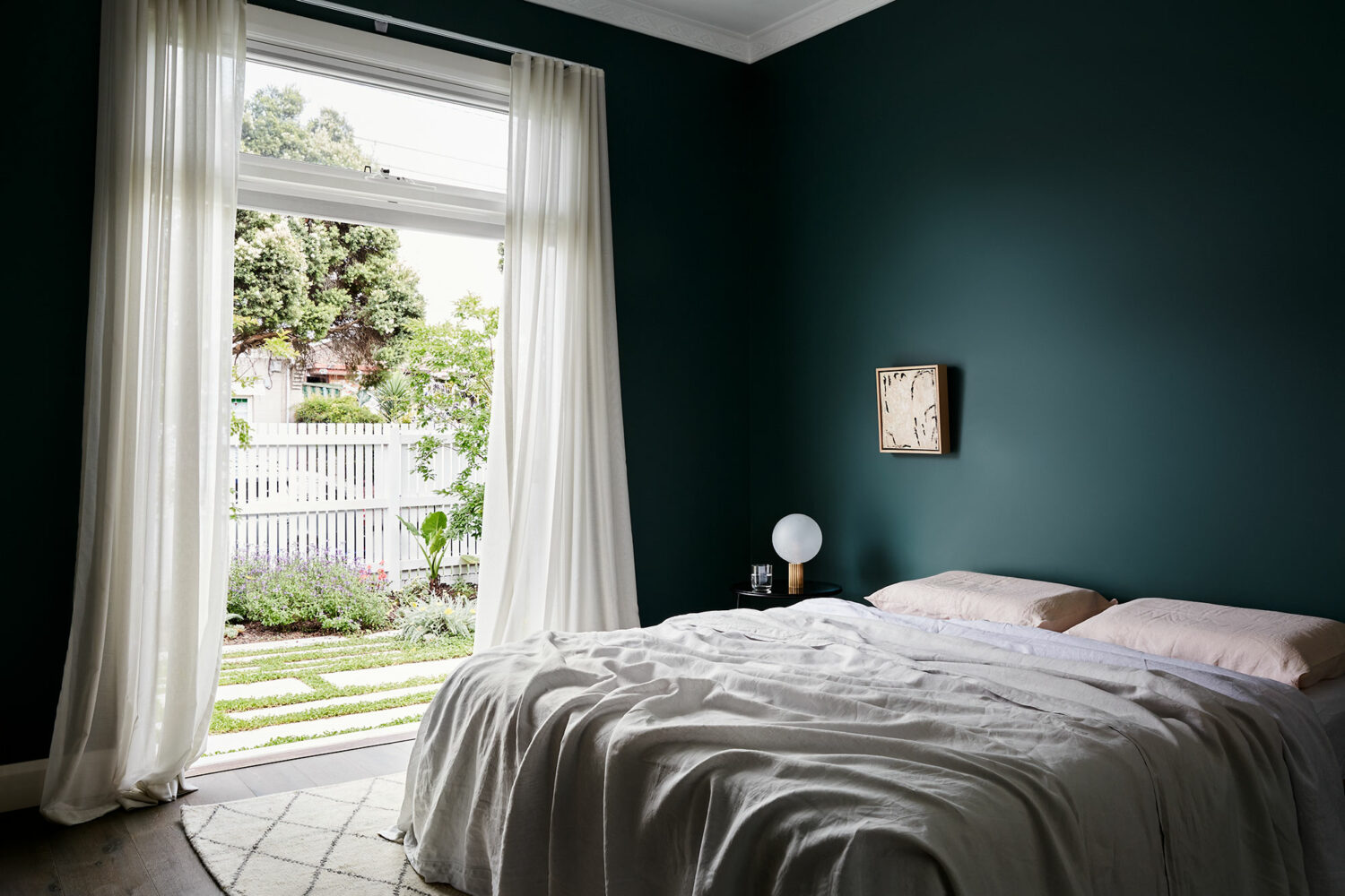 Maike Design dark teal bedroom opening onto private courtyard. Linen sheets and artwork.