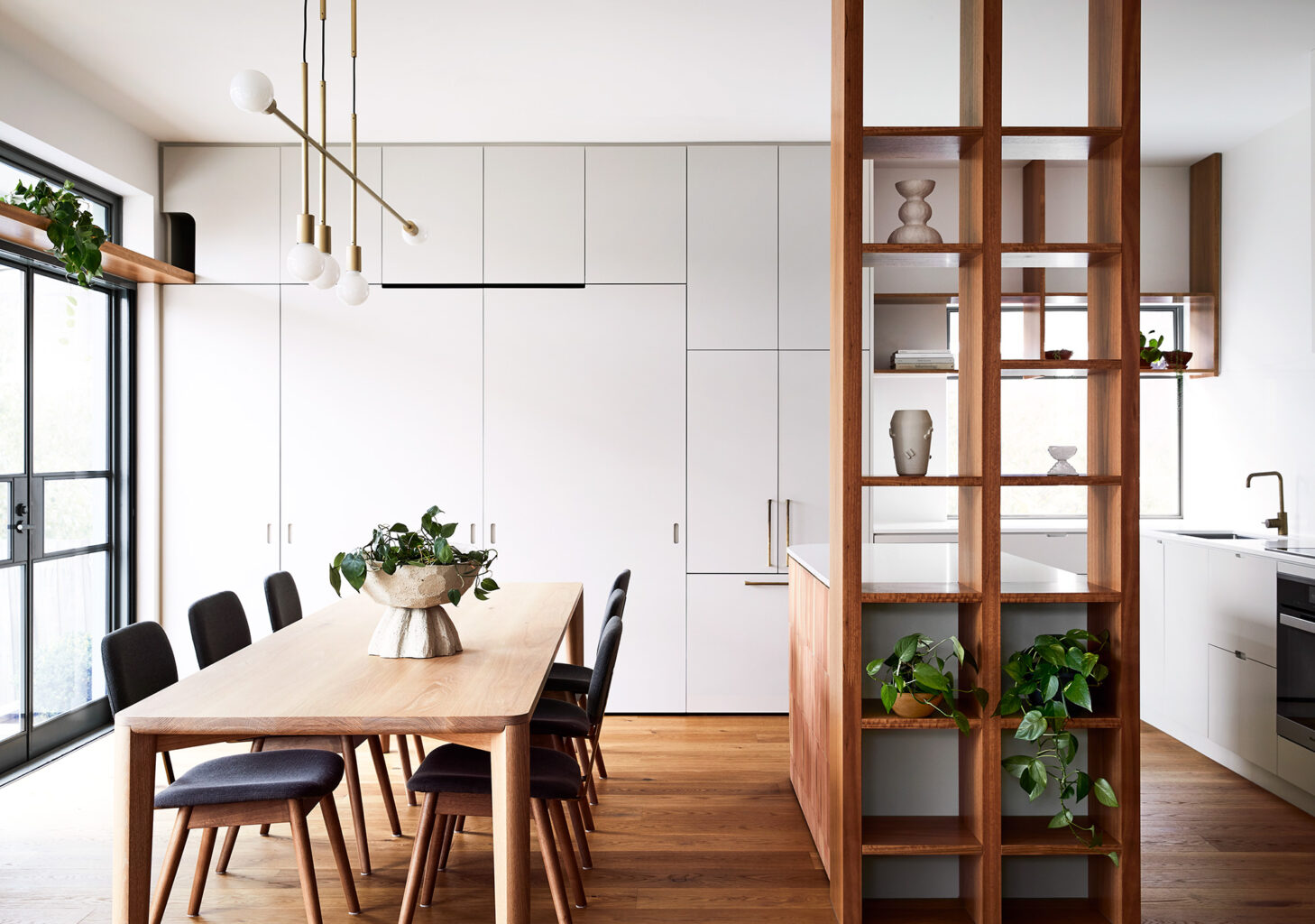 Maike Design kitchen and dining room. Open timber shelves, indoor plants, brass pendant light, teracotta tiles, timber floors.