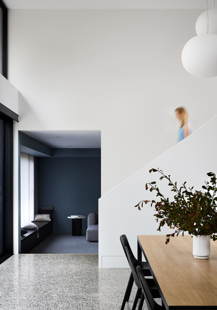 Maike Design dining room. Double height space with polished concrete floor. View through to blue painted lounge room